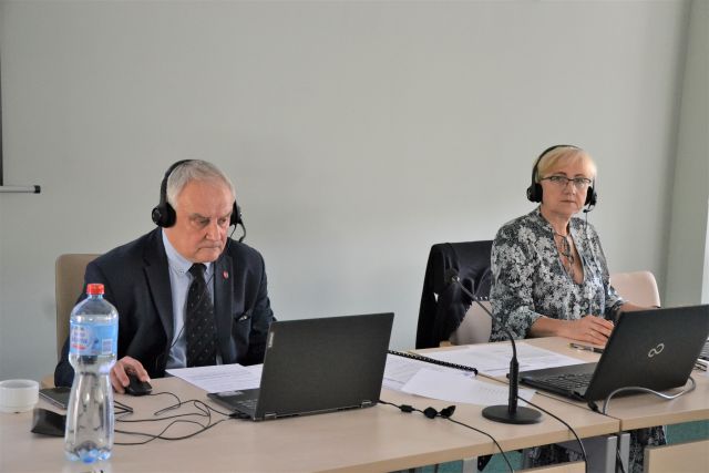 na zdjęciu widoczne są dwie osoby siedzące przy jednym stole. Od lewej - przewodniczący rady powiatu skarzyskiego jacek Jeżyk i wiceprzewodnicząca Bożena Bętkowska. Przed kobieta i mężczyzną stoją laptopy. Obydwoje mają założone słuchhawki. Znajdują się w powiatowej sali obrad     